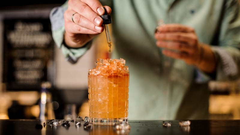 A person dropping some bitters into a cocktail