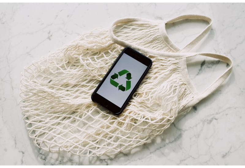 A phone displaying the recycling symbol resting on an eco bag