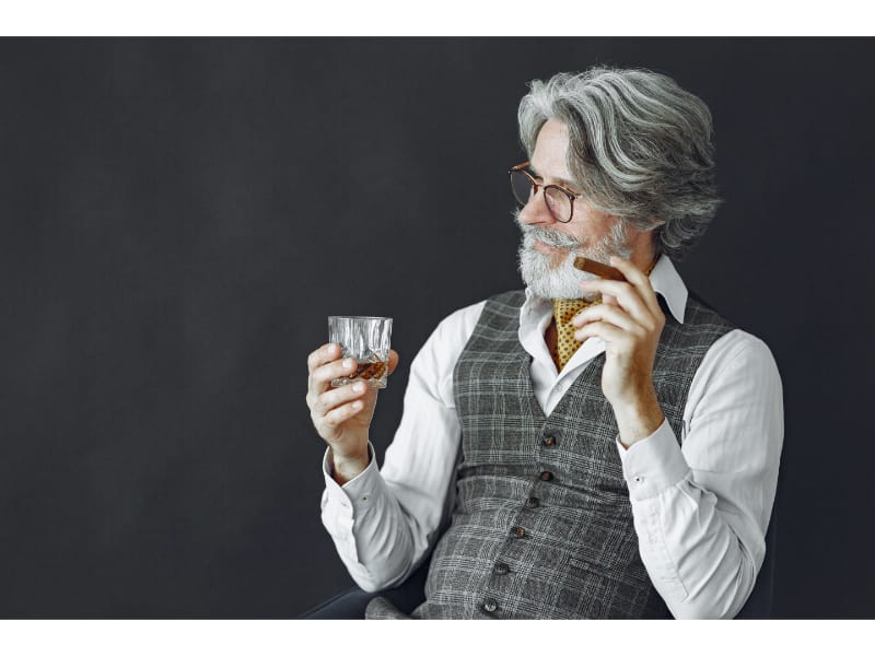 An old man holding a glass of whiskey by the base