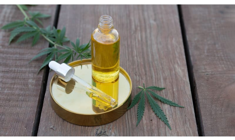 Glass Bottle Dropper of Cannabis Oil with Leaves Wooden Planks