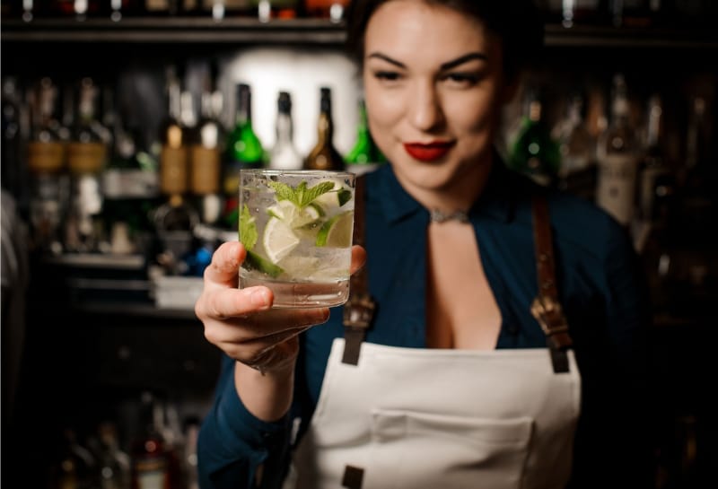 Bartender girl holding an fresh cocktail with lime and mint