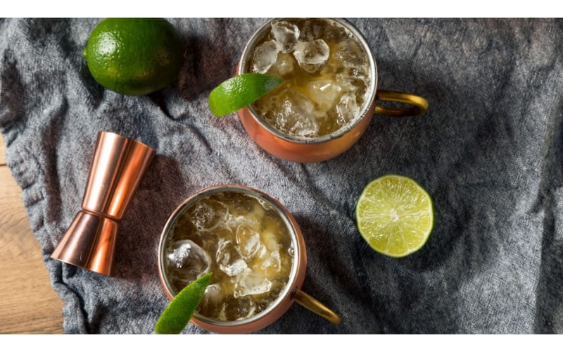 Bourbon mule served in copper mugs with lime slices and a jigger on the side