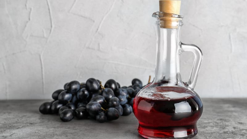 Glass jug with wine vinegar and fresh grapes on gray table