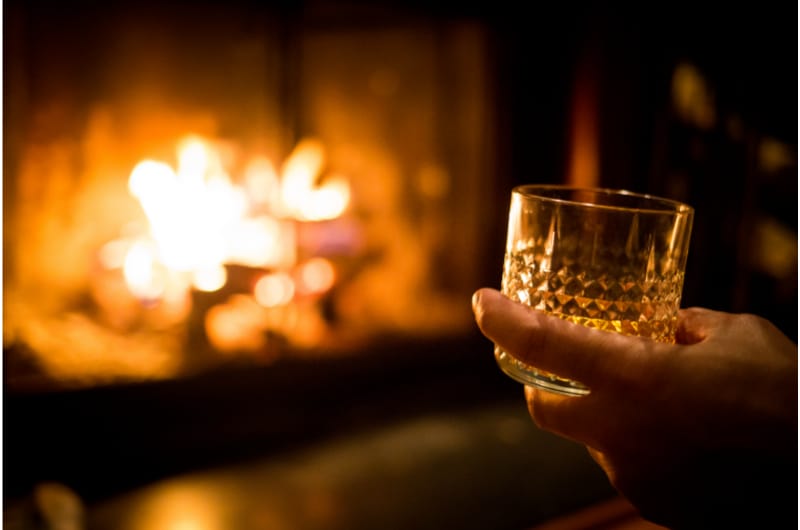 Hand holding whiskey glass at the fireplace