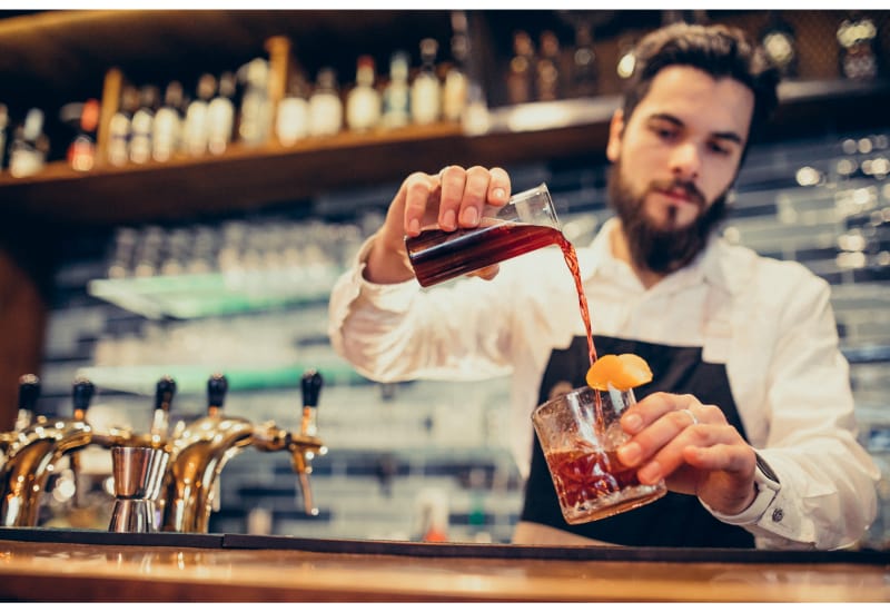 Man bartending and pouring cocktail in a glass
