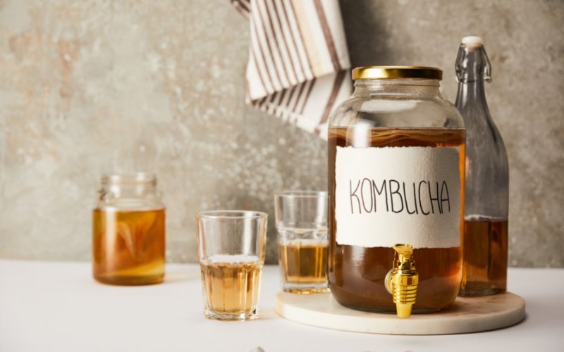Jar with kombucha near glasses and bottle on textured grey background