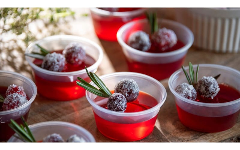 Jello shots on plastic cups and garnished with frozen berries