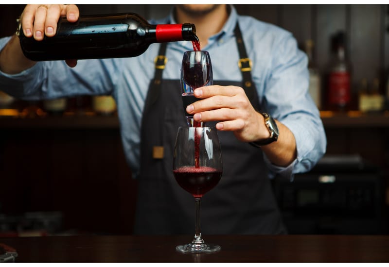 Male sommelier pouring red wine through aerator into glass