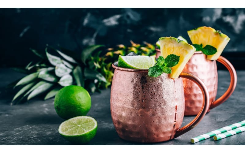 Pineapple Moscow mule served in two copper mugs garnished with pineapple slices and lime