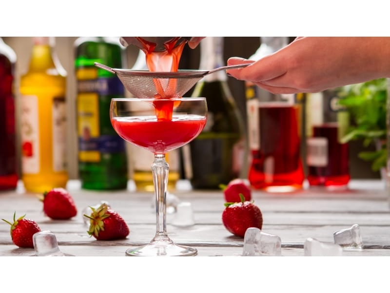 Red cocktail poured through a sieve into a coupe glass