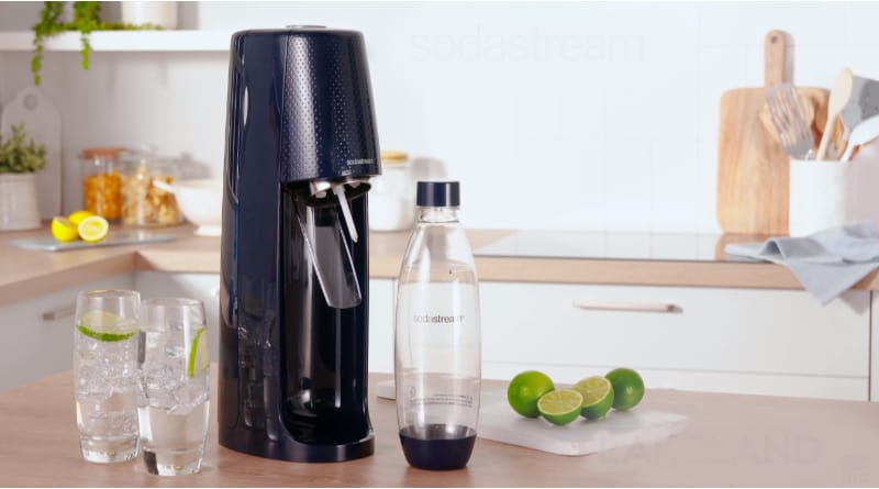 SodaStream on a kitchen counter with two glasses and limes on a chopping board