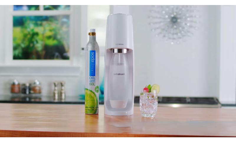 SodaStream White in between a CO2 canister and glass on a table