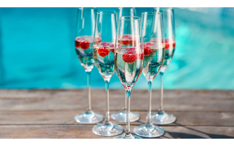 Champagne with raspberries in flute glasses by the pool.