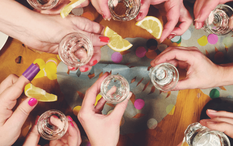 Group of people holding shots of tequila with slices of lemon