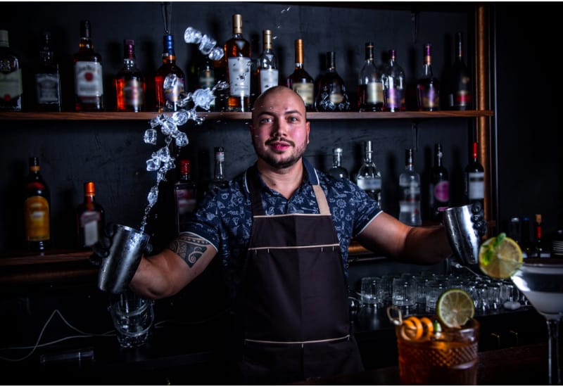 The barman juggler throws up an ice for cocktail at bar