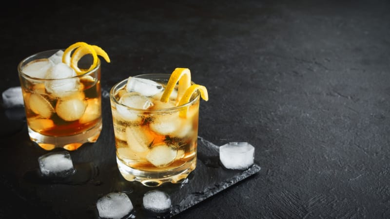 Two glasses of gold rum with lemon shavings and ice cubes