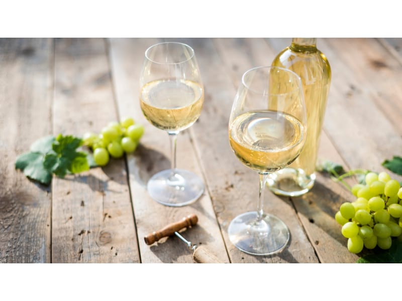 Two glasses of white wine with the bottle and grapes