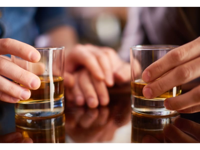 Two people holding a glass of whiskey by the body