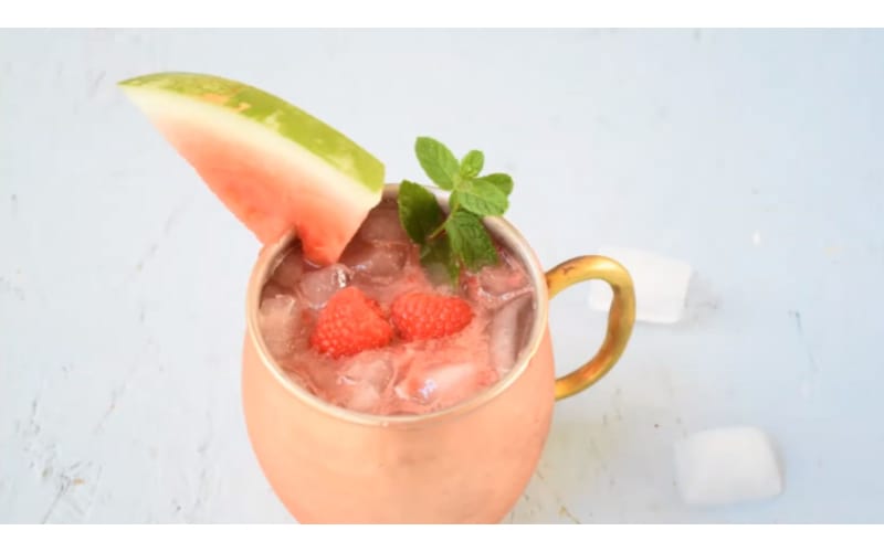 Watermelon Moscow mule served in a copper mug garnished with a watermelon slice and raspberries 