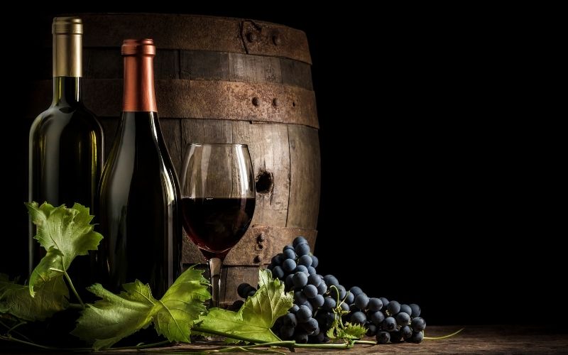 A wine barrel, two bottles of wine, and a glass of wine with grapes in the background