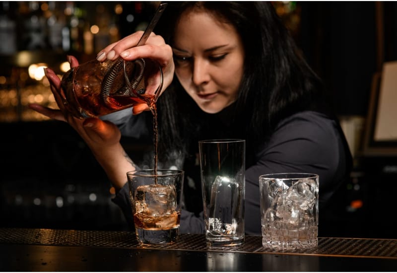 woman bartender pours alcoholic cocktail into glass