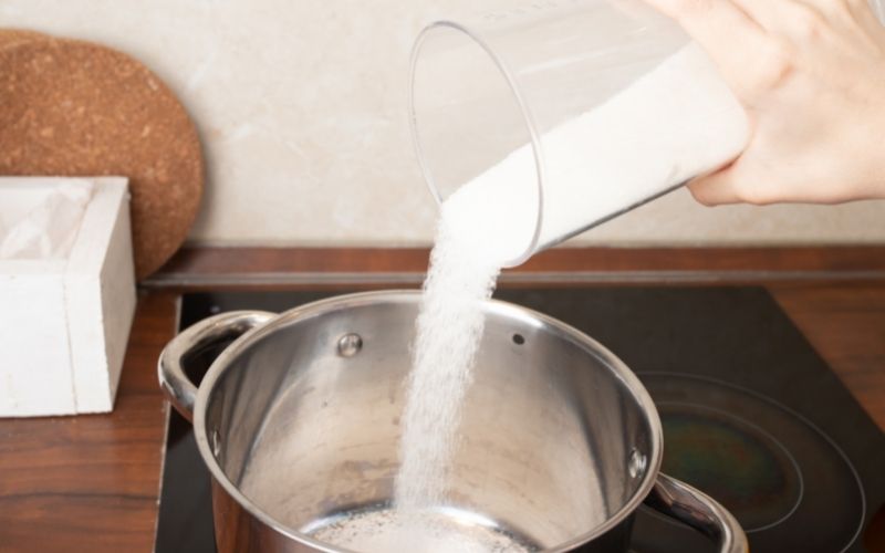 woman's hands pouring sugar into a saucepan
