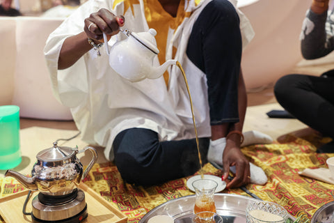 Maimouna Kanté, fondatrice de Kanté, une femme qui verse du thé vert dans une tasse en créant une mousse blanche délicate dans le cadre du rituel africain de l'Ataya