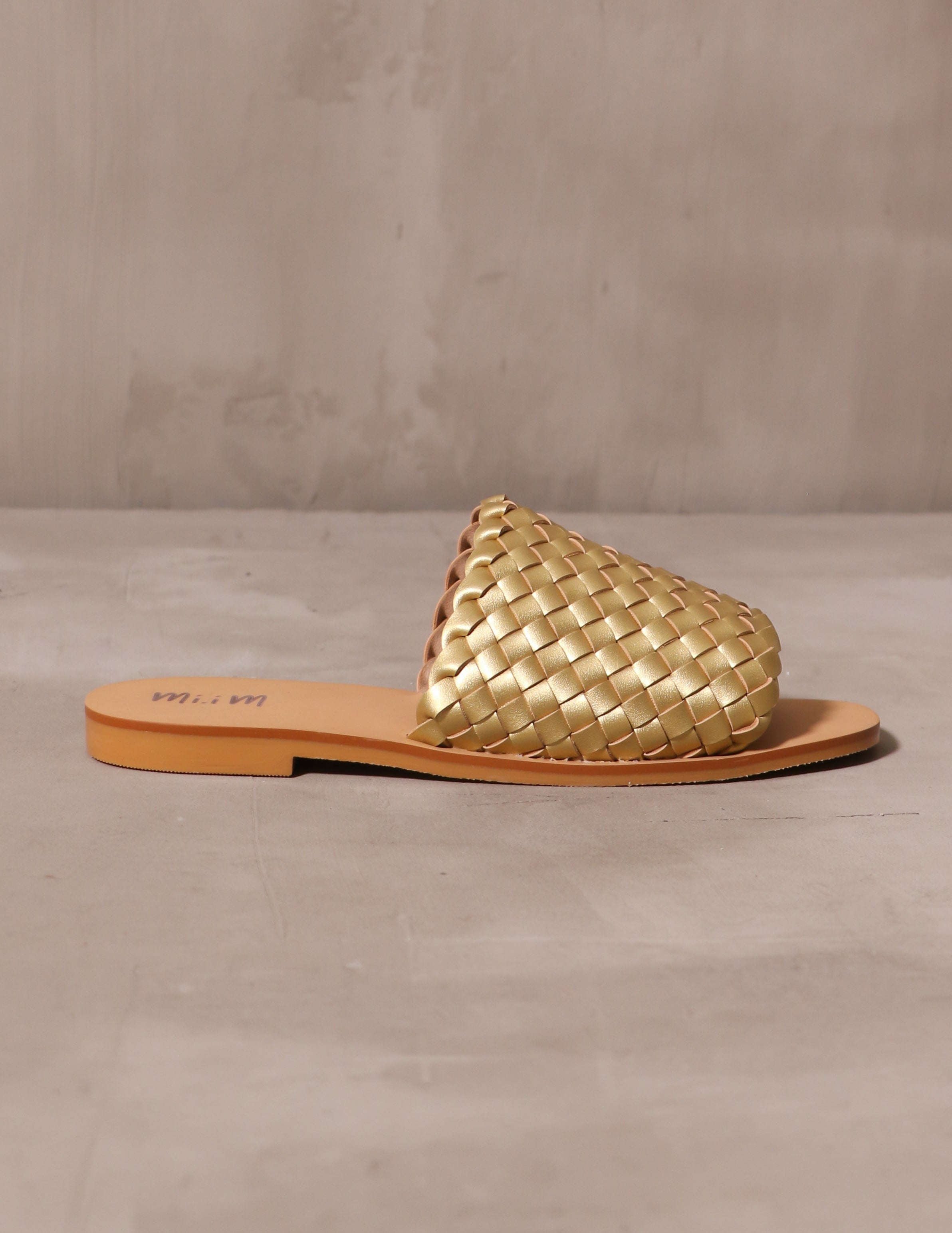 gold woven one slide sandal on cement background