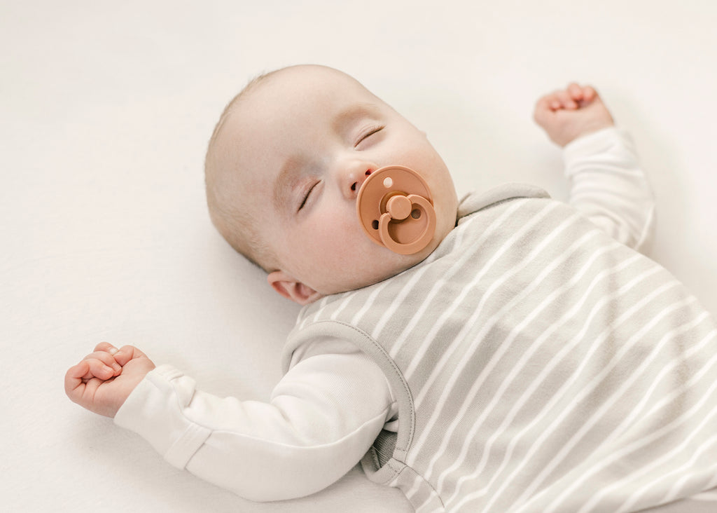 Baby sucking on pacifier while asleep on back in a Woolino sleep sack. Baby Twitching In Sleep, Should You Be Worried, Experts Weigh In.