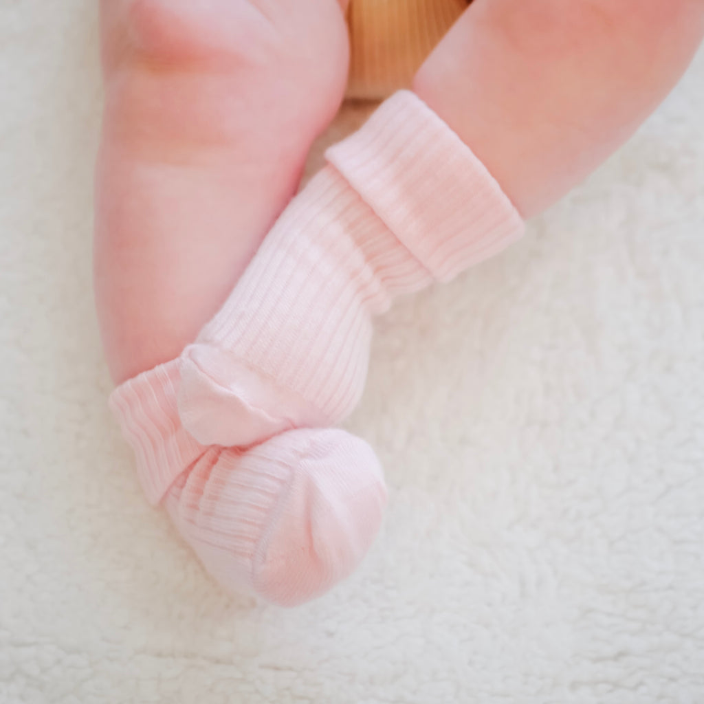 Baby feet dressed in cozy pink Woolino merino wool baby socks.