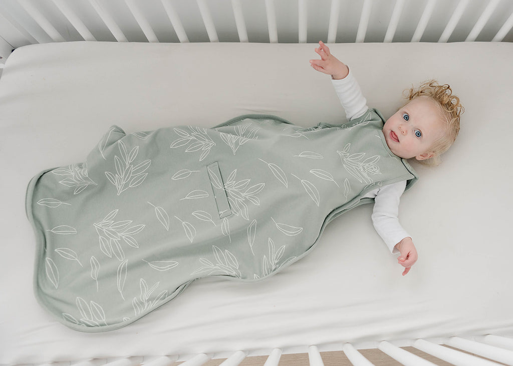Baby lying in crib wearing a Woolino 4 Season® Ultimate Baby Merino Wool Sleep Bag in Sage print