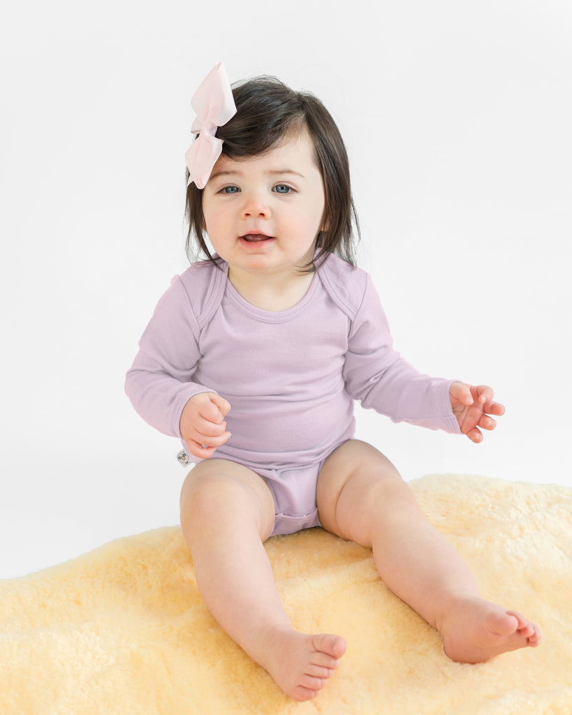 Baby sitting on lambskin rug and wearing a Woolino merino wool bodysuit in Lilac