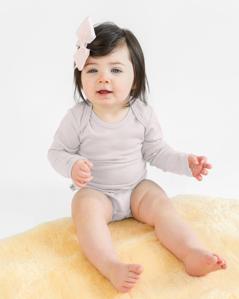 Baby sitting on lambskin rug dressing in a beige Woolino merino wool bodysuit