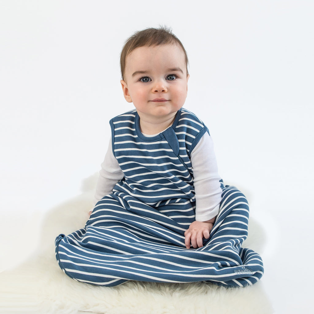 Baby sitting on lambskin rug wearing a Woolino 4 Season Basic Merino Wool Sleep Bag in Navy Blue stripes