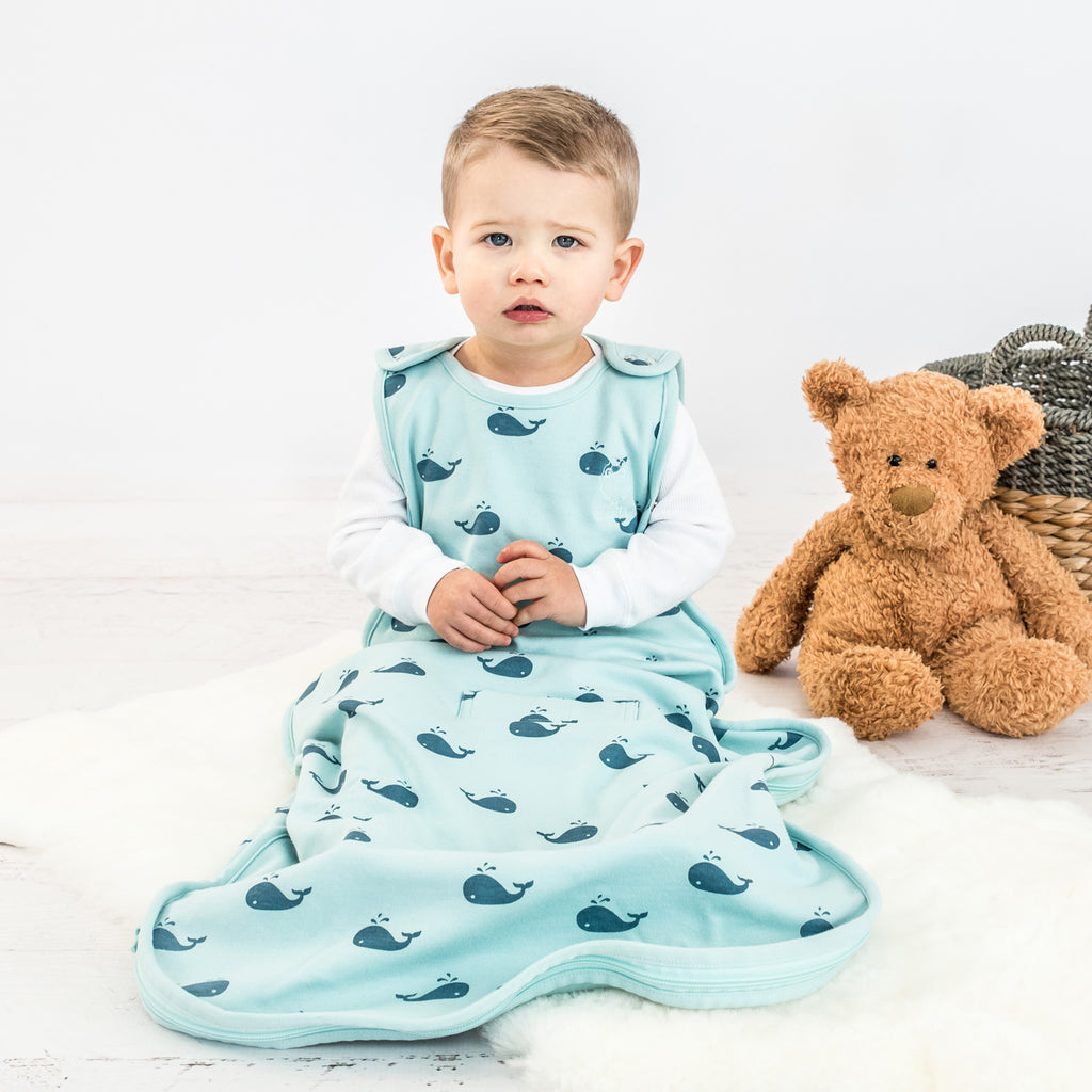 Baby sitting on lambskin rug wearing a Woolino 4 Season® Ultimate Baby Sleep Bag in Whales print