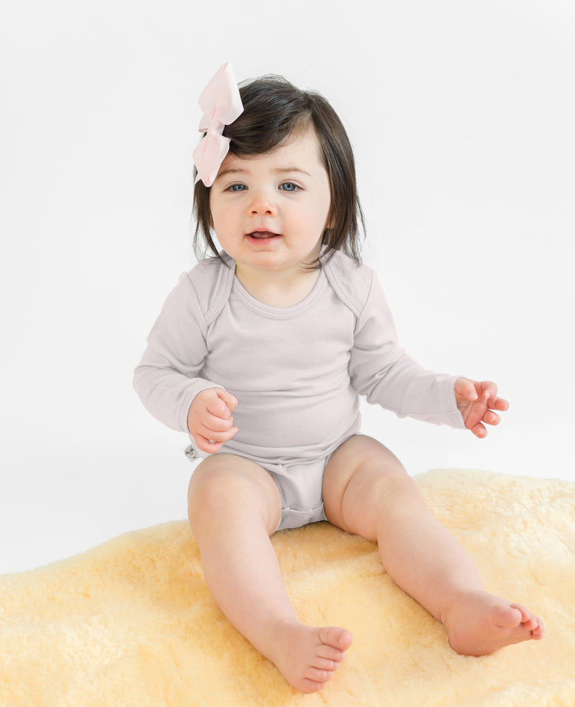 Baby sitting on lambskin rug wearing a Woolino merino wool bodysuit.
