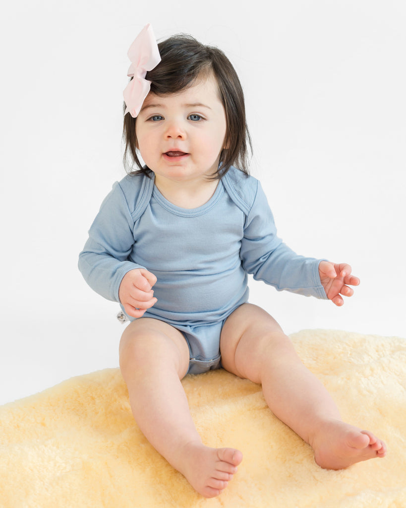 Baby sitting on lambskin rug wearing a Woolino merino wool bodysuit in blue