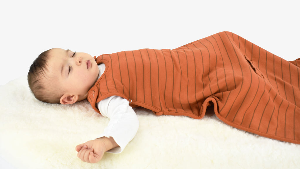 Baby sleeping on lambskin rug, wearing a Woolino 4 Season® Ultimate Baby Sleep Bag in Rust