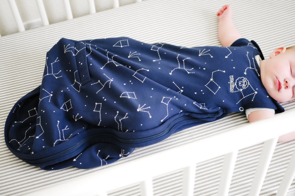 Baby sleeping safely on back in crib wearing a Woolino 4 Season Ultimate merino wool sleep bag in Night Sky print.