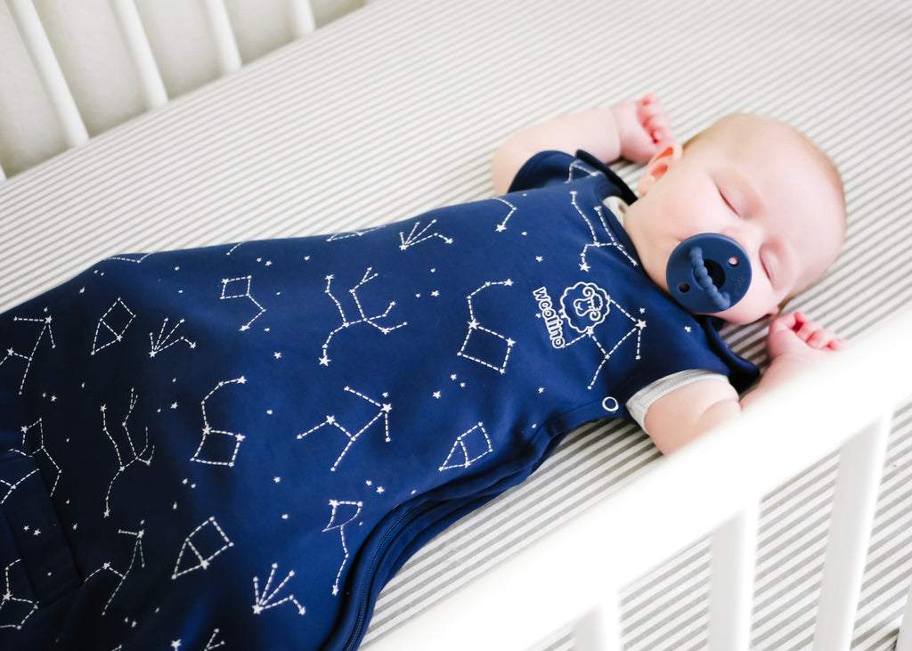 Baby sleeping with pacifier in crib while wearing a Woolino 4 Season Ultimate Sleep Bag in Night Sky print.