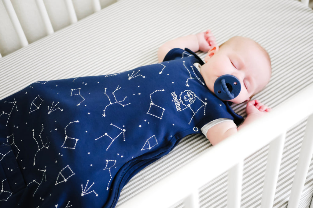 Baby with pacifier asleep on back in crib wearing a Woolino 4 Season® Ultimate Baby Sleep Bag in Night Sky print