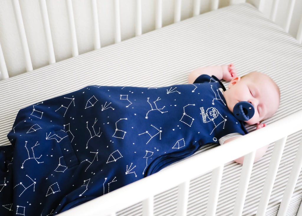 Baby with pacifier sleeping on back in a crib wearing a Woolino 4 Season® Ultimate Baby Sleep Bag