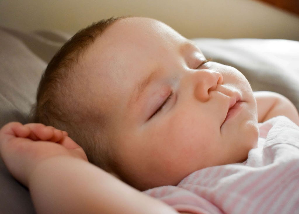 Close-up of baby’s face with arms next to the head, lying on back, asleep. Baby Twitching In Sleep.