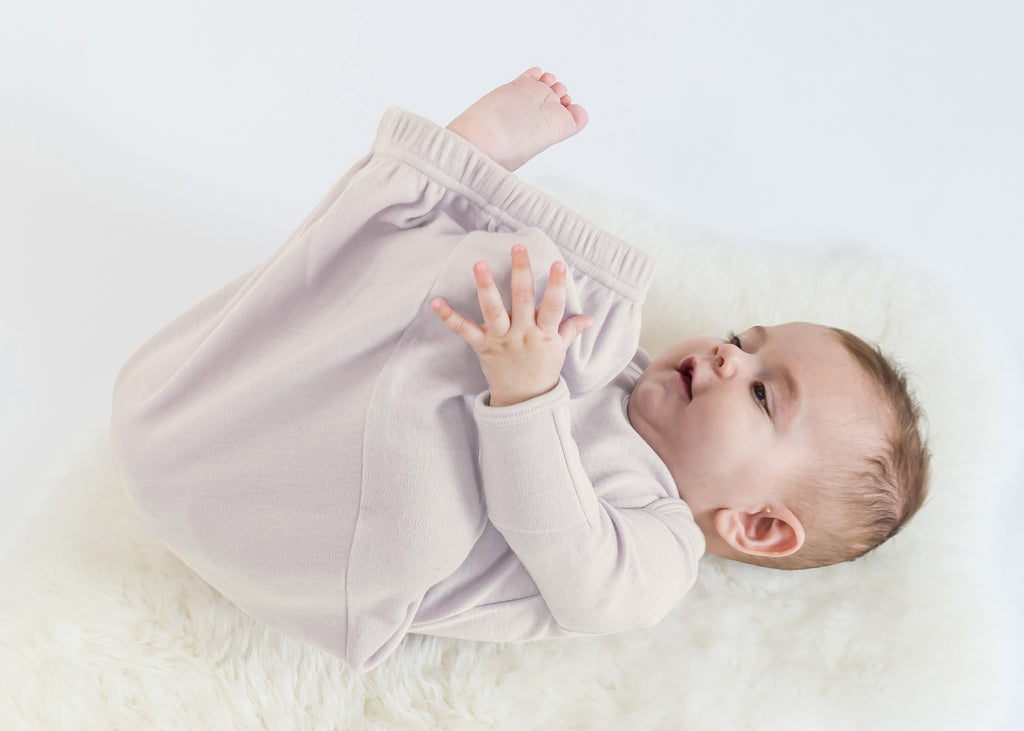 Happy baby discovering their feet while wearing a Woolino merino wool baby gown.