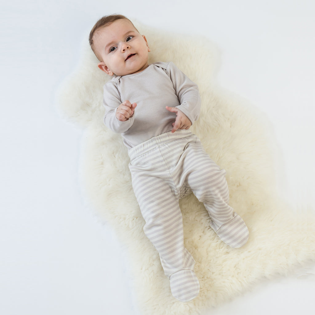 Happy baby laying on lambskin rug dressed in Woolino merino wool Bodysuit and Footed Pants