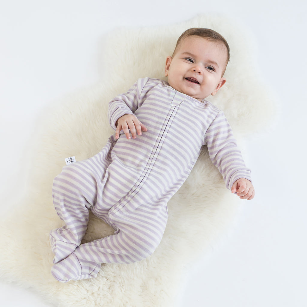 Happy baby laying on lambskin rug wearing a Woolino merino wool footie pajama sleeper in lilac stripes.