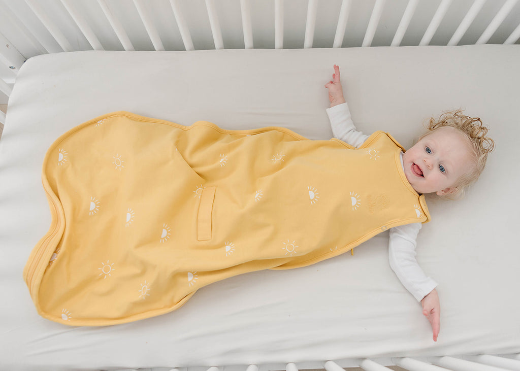 Happy baby on back in crib wearing a yellow Woolino 4 season Ultimate sleep sack in Sun print, How to Keep Your Baby Warm at Night