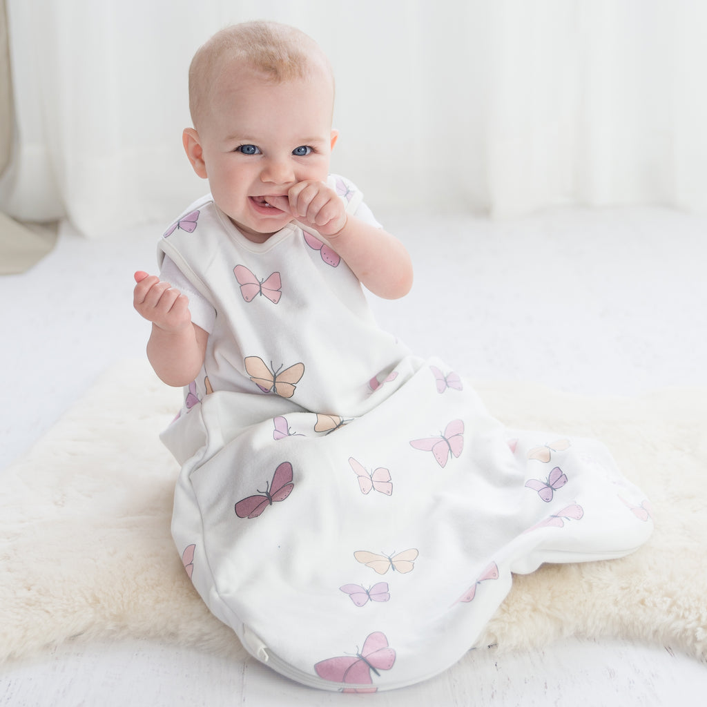 Happy baby sitting on lambskin rug wearing a Woolino 4 Season® Basic Baby Sleep Bag in Butterfly print