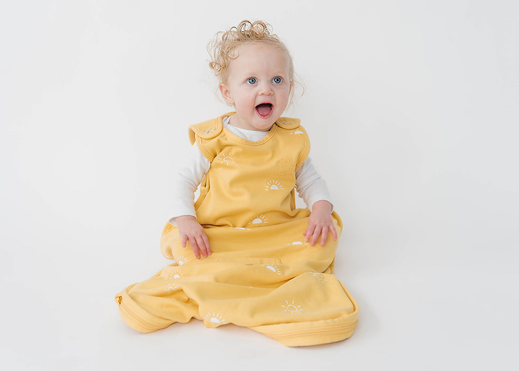 Happy baby sitting up while wearing a yellow Woolino 4 Season® Ultimate merino wool baby sleep bag in Sun print