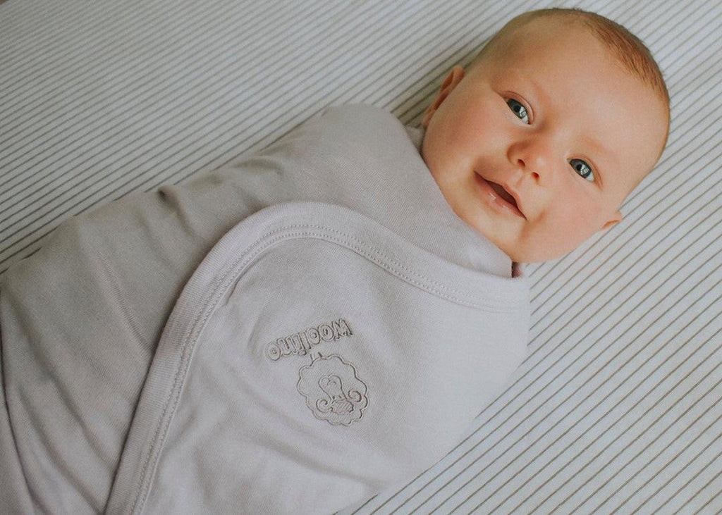 A happy baby swaddled in a Woolino merino wool swaddle blanket